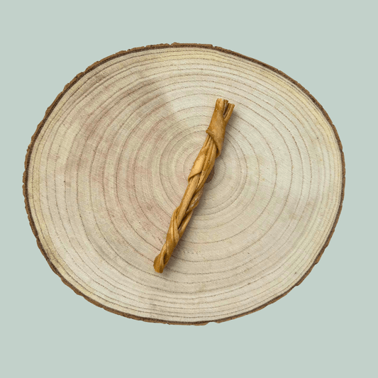 Single braided lamb skin chew for dogs on a wood slice plate against a jade green background