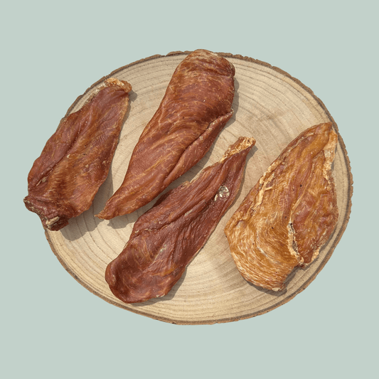 4 dried chicken fillet natural and healthy dog chews on a wooden slice plate against a jade green background