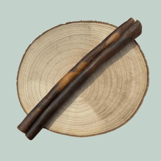 A single roll of dried camel skin natural and healthy chews for dogs on a wood slice plate against a jade green background