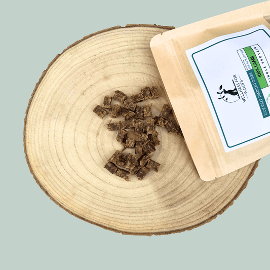 A pouch of single protein pure lamb meat training treats for dogs. The pouch is lay on a wooden slice plate beside a pile of the treats.