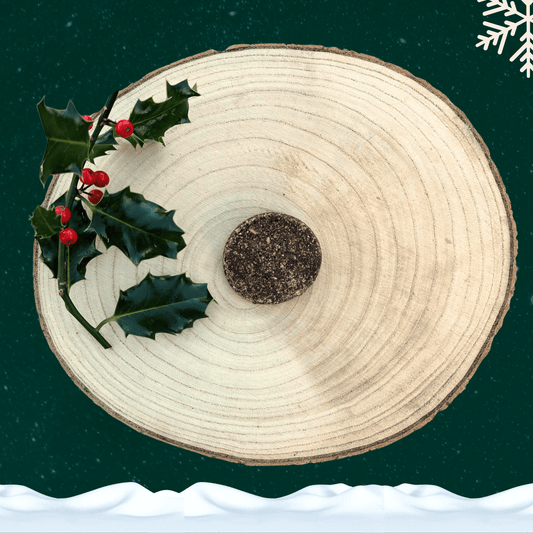 A single pheasant and partridge cookie for dogs on a wooden slice plate next to a sprig of holly. All on a starry green background with a white snowflake in the top right hand corner and a blanket of snow across the bottom.