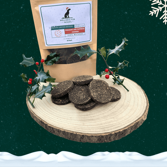 Pile of pheasant and partridge cookies for dogs on a wooden slice plate next to a filled pouch of 10 cookies. All on a starry green background with a white snowflake in the top right hand corner and a blanket of snow across the bottom.