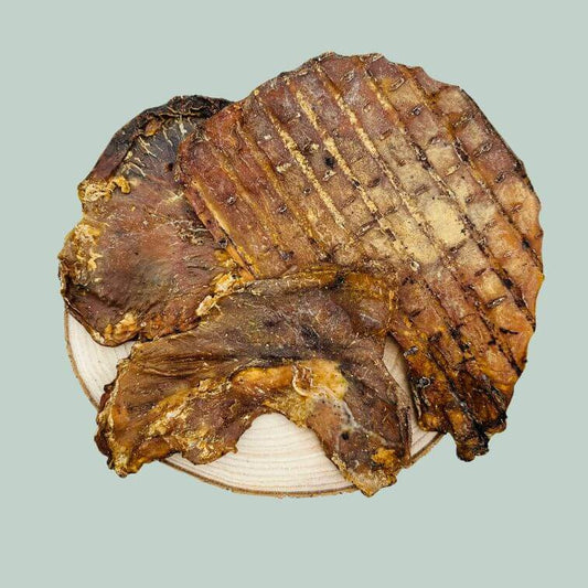 3 dried pig stomach dog treats on a wooden slice plate and jade green background