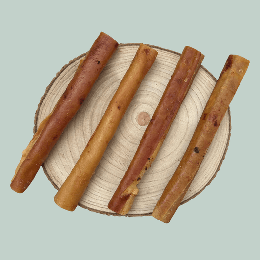 Four pork rind roll natural dog treats on a wooden slice plate against a jade green background.
