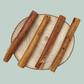 Four pork rind roll natural dog treats on a wooden slice plate against a jade green background.
