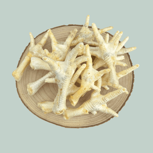 Pile of dried and puffed chicken feet for dogs and puppies on a wooden slice plate against a jade green background