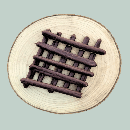 10 guinea fowl sausage dog treats stacked neatly on a wooden plate.