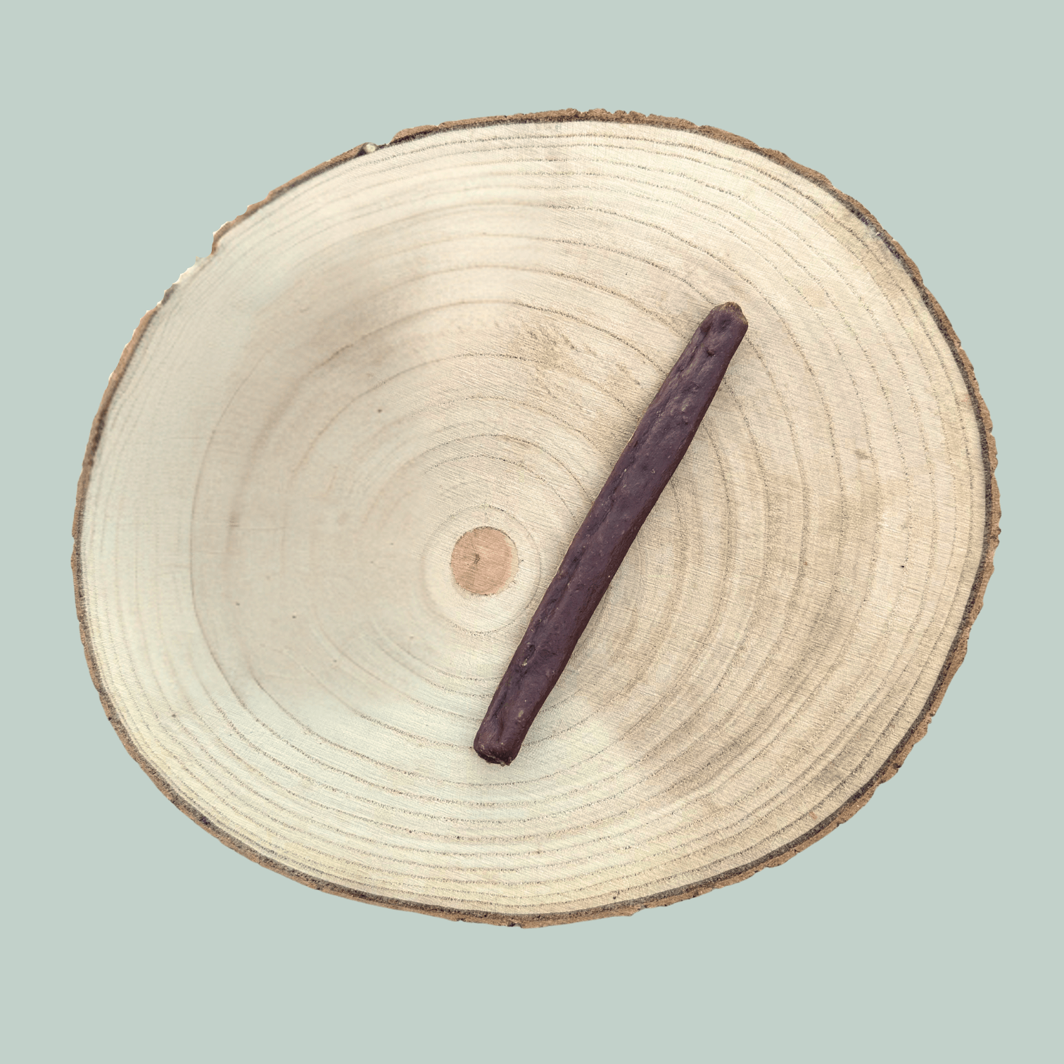 A single guinea fowl sausage dog treat on a wooden plate next to a piece of holly.