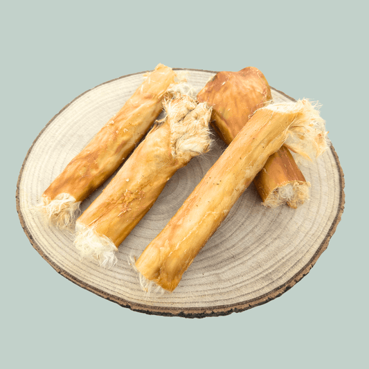 Rolls of furry dried rabbit skin healthy treat for dogs on a wooden slice plate against a jade green background.