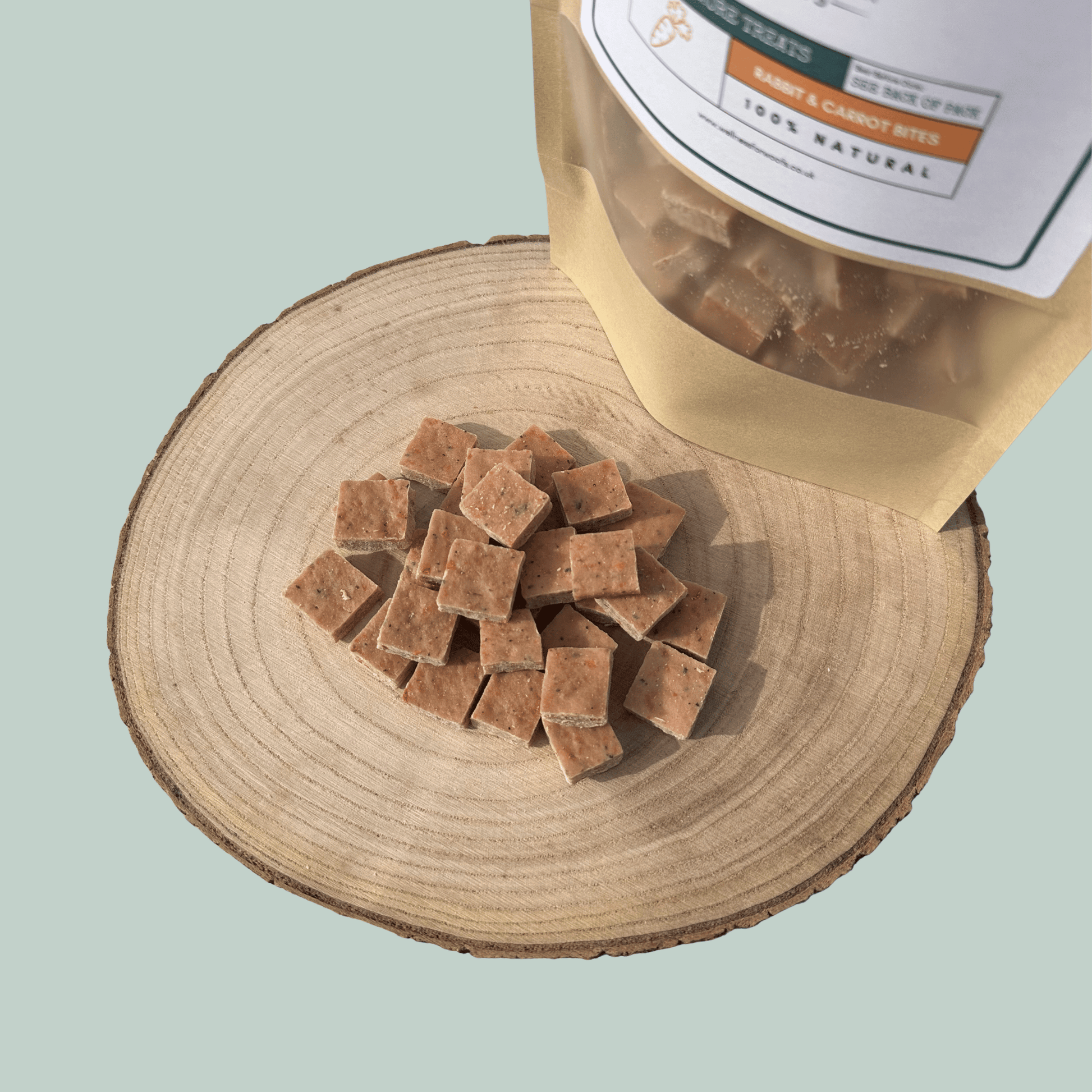 Dog treats on a wooden surface with a packaging bag labeled 'Rabbit & Carrot Bites'.