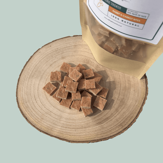 Dog treats on a wooden surface with a packaging bag labeled 'Rabbit & Carrot Bites'.