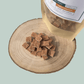 Dog treats on a wooden surface with a packaging bag labeled 'Rabbit & Carrot Bites'.