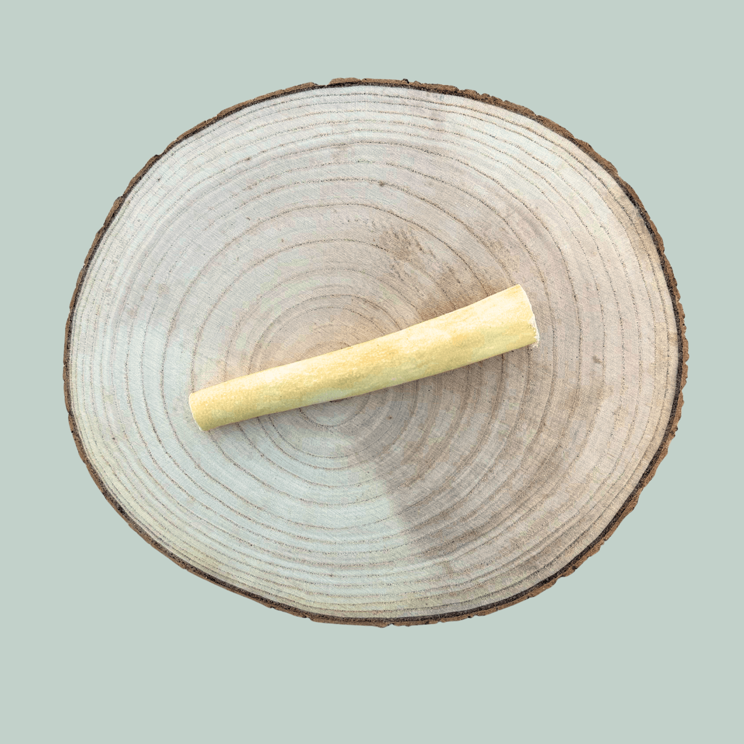 Single buffalo tail piece natural dog chew for dogs on a wooden slice plate against a jade green background.