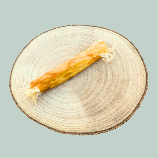 Single rabbit skin roll healthy dog chew on a wooden slice plate against a jade green background.