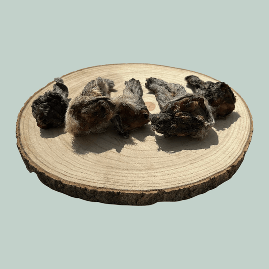 Side view of 5 Small Furry Lamb Ear dog treats on a wooden slice plate against a jade green background