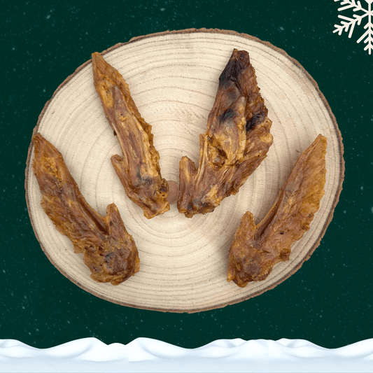 4 dried turkey wing dog chews on a wooden slice plate against a dark green starry background with a white snowflake in the top right corner and a blanket of snow across the bottom.