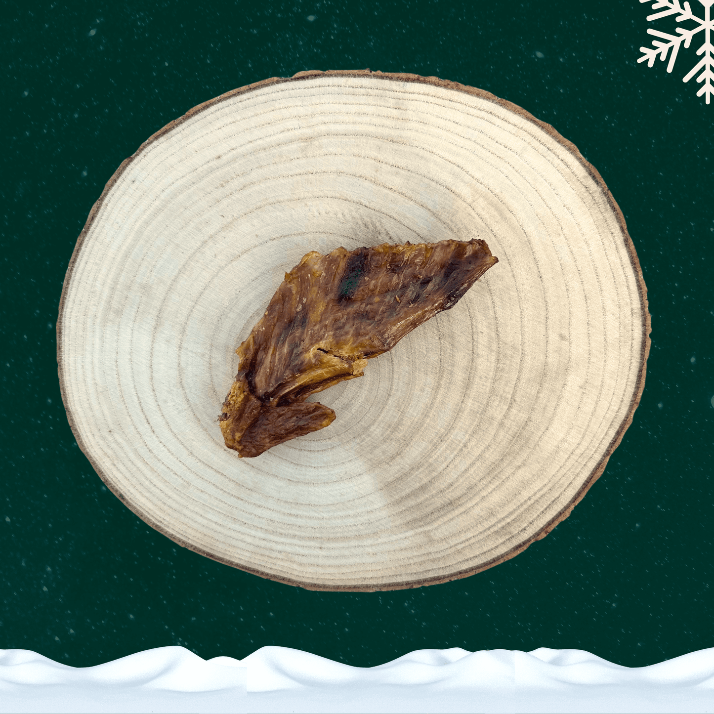 A single dried turkey wing dog chew on a wooden slice plate against a dark green starry background with a white snowflake in the top right corner and a blanket of snow across the bottom.