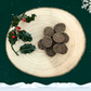 Pile of Turkey and Cranberry Biscuits for dogs on a wooden plate next to a sprig of holly. All set on a dark green starry background with a white snowflake in the top right corner and a blanket of snow across the bottom.