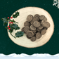 Pile of Turkey and Cranberry Biscuits for dogs on a wooden plate next to a sprig of holly. All set on a dark green starry background with a white snowflake in the top right corner and a blanket of snow across the bottom.