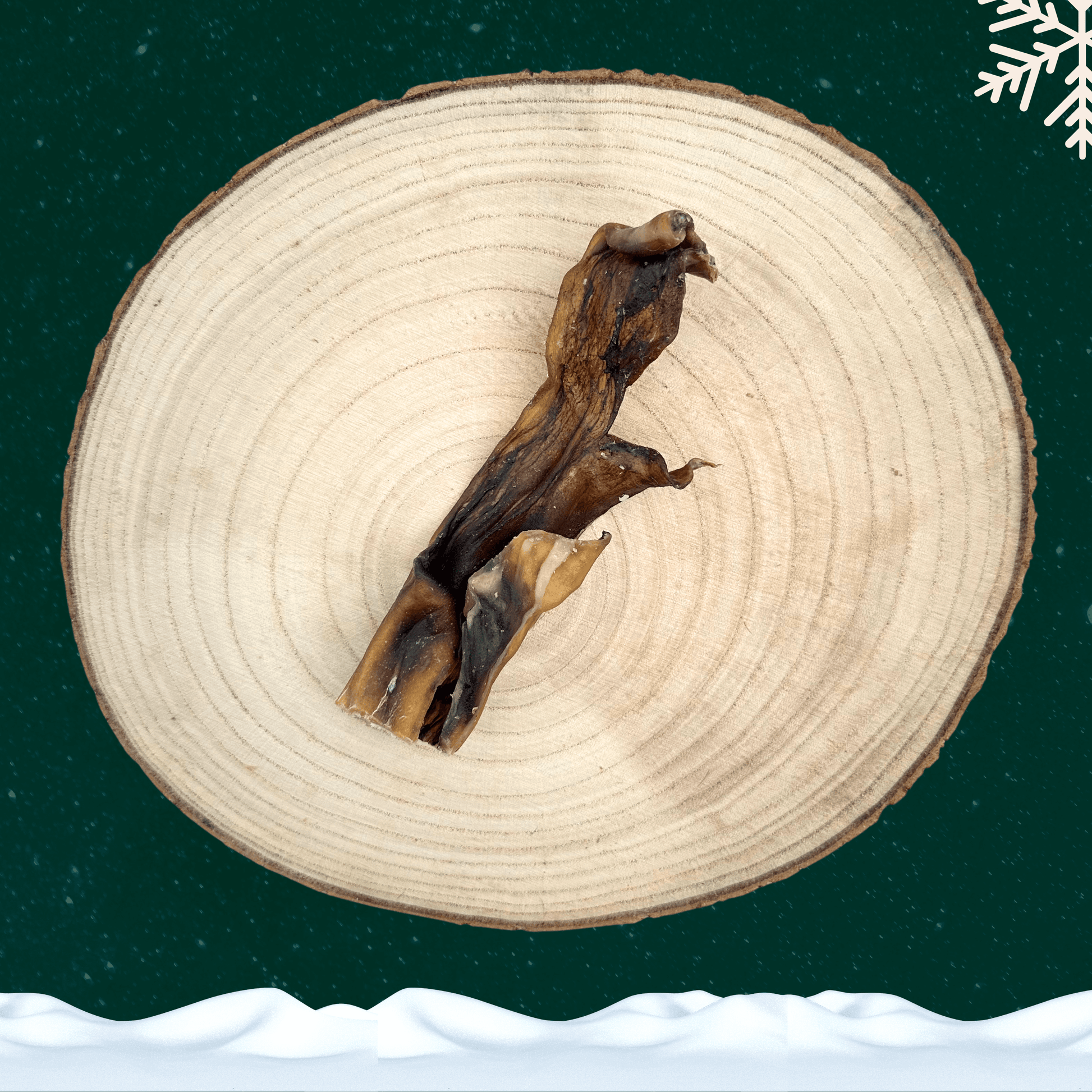 A slice of venison skin chew for dogs on a wooden plate against a dark green starry sky background. There is a white snowflake in the top right corner and a blanket of snow across the bottom.