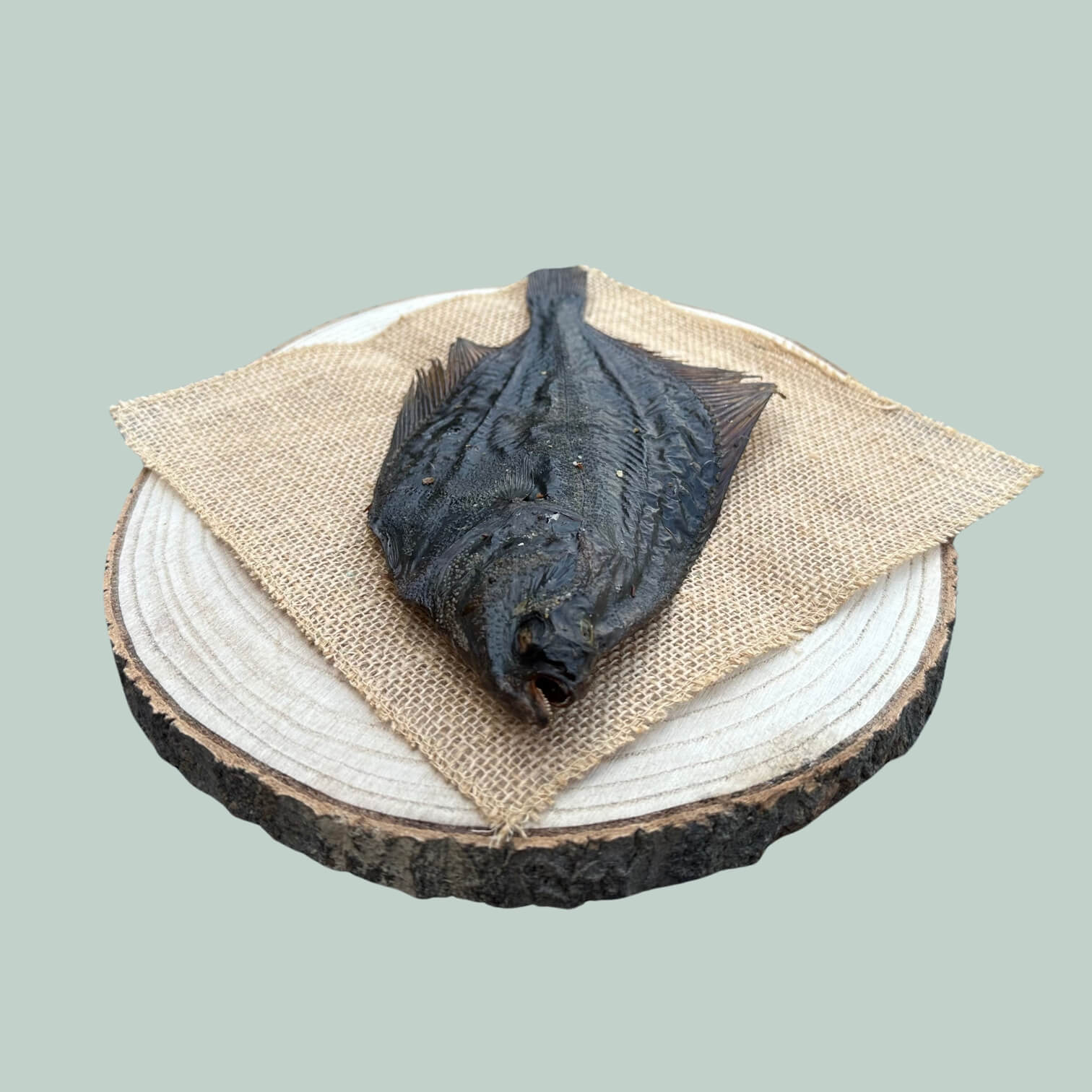 Side view of a whole dried flounder treat for dogs on a wooden plate